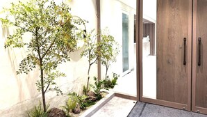 Una entrada moderna con una puerta de madera, un pequeño jardín interior y un camino de hormigón que lleva a una puerta de cristal.