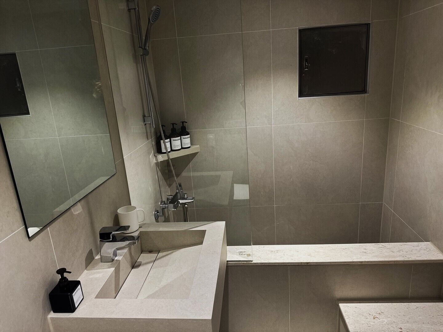 A modern bathroom with a large mirror, a sink with a soap dispenser, a shower area, and a toilet.