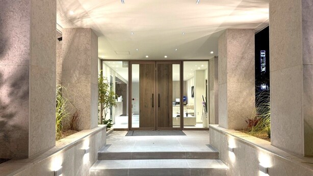 Una entrada de hotel moderna con un puerta de cristal, escalones que llevan a ella, y un interior bien iluminado visible a través del cristal.