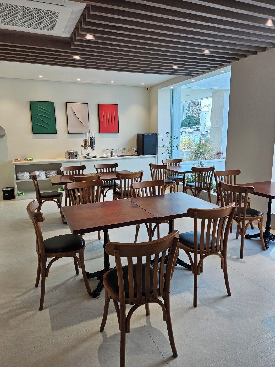 Un espace repas moderne avec des tables et des chaises en bois, un comptoir de cuisine et des œuvres d’art accrochées aux murs.