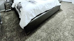 Un dormitorio con cabecera capitonada, una cama grande con ropa de cama blanca, un ventilador de techo, una mesita de noche con lámpara y un aparador con espejo.