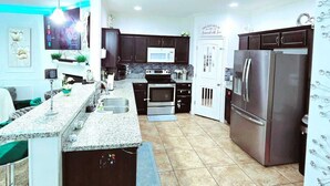 Una cocina moderna con armarios oscuros, un refrigerador de acero inoxidable, horno empotrado y encimera de granito.