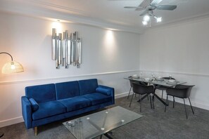 A modern living room with a blue sofa, a glass coffee table, a dining table with chairs, and a wall-mounted light fixture. - 2-bedroom- Stoke-on-Trent-Sleeps 5-PetsOk (Stoke-on-Trent)
