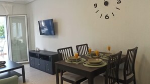 A dining area with a table set for four, a wall clock, and a flat-screen TV mounted on the wall. - 2 Bed Apt - Close To Beach - Pool - Balcony (Mojacar)