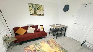 A living room with a red sofa, a coffee table, a dining table with chairs, a colorful rug, and a painting on the wall. - Central Chelmsford 2-Bed Apt, 5 mins to Station (Chelmsford)
