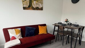A red sofa with three pillows, a dining table with four chairs, and a painting on the wall. - Central Chelmsford 2-Bed Apt, 5 mins to Station (Chelmsford)
