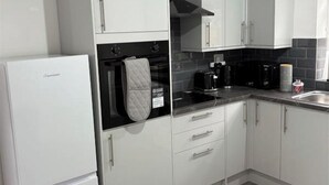 A modern kitchen with white cabinets, a black oven, and a stainless steel sink. - Central Chelmsford 2-Bed Apt, 5 mins to Station (Chelmsford)