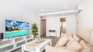 Un salon moderne avec un téléviseur à écran plat, un canapé beige, une table basse et une plante en pot.