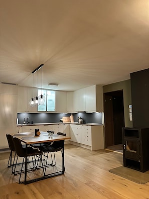 A modern kitchen with a dining area, featuring a wooden table, black chairs, and a black countertop.