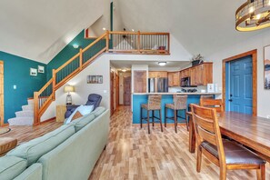 A multi-level living space with a staircase, a dining area with wooden chairs, a kitchen with modern appliances, and a blue accent wall. - 3-bedroom Cabin 13 in Bridges Bay, with on site eating and in/outdoor pool. (Arnolds Park)