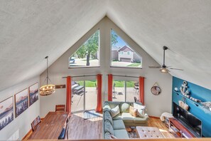 A spacious loft with a high ceiling, large windows, a dining area, a sofa, and a TV. - 3-bedroom Cabin 13 in Bridges Bay, with on site eating and in/outdoor pool. (Arnolds Park)