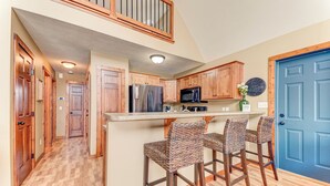 A kitchen with wooden cabinets, a stainless steel refrigerator, a microwave, and a bar area with wicker chairs.