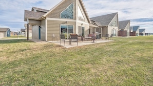 A modern single-story house with a large patio area, a covered outdoor seating area, and a fenced backyard.