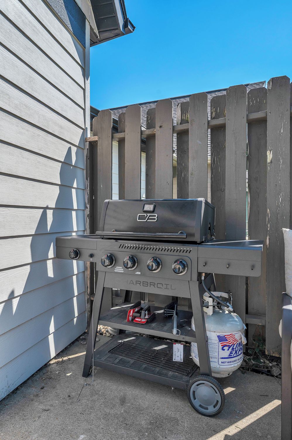 Una parrilla portátil para barbacoa con cuatro perillas de control, un tanque de combustible y una cadena para facilitar su transporte.