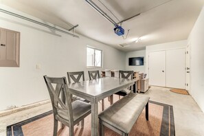 Een ruime kamer met een grote eettafel, stoelen, een bank en een flatscreen-tv aan de muur, plus een plafondprojector.