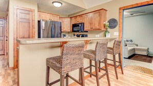 A kitchen with wooden cabinets, a stainless steel refrigerator, a microwave, and three wicker bar stools.