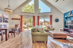 A spacious living room with a high ceiling, a dining area, and a large TV.