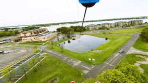 An aerial view of a parking lot with a large building, a grassy area, and a body of water in the background. - 3-bedroom Cabin 13 in Bridges Bay, with on site eating and in/outdoor pool. (Arnolds Park)