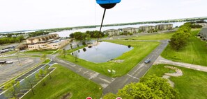 An aerial view of a parking lot with a large building, a grassy area, and a body of water in the background.