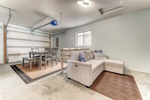 Een ruime kamer met een groot raam, een witte bank, een eettafel met stoelen en een garagepoort.