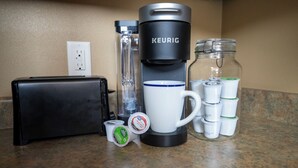 A coffee maker, a mug, a thermos, a glass jar, and a black case on a kitchen counter. - 3-bedroom Cabin 13 in Bridges Bay, with on site eating and in/outdoor pool. (Arnolds Park)