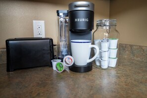 A coffee maker, a mug, a thermos, a glass jar, and a black case on a kitchen counter.