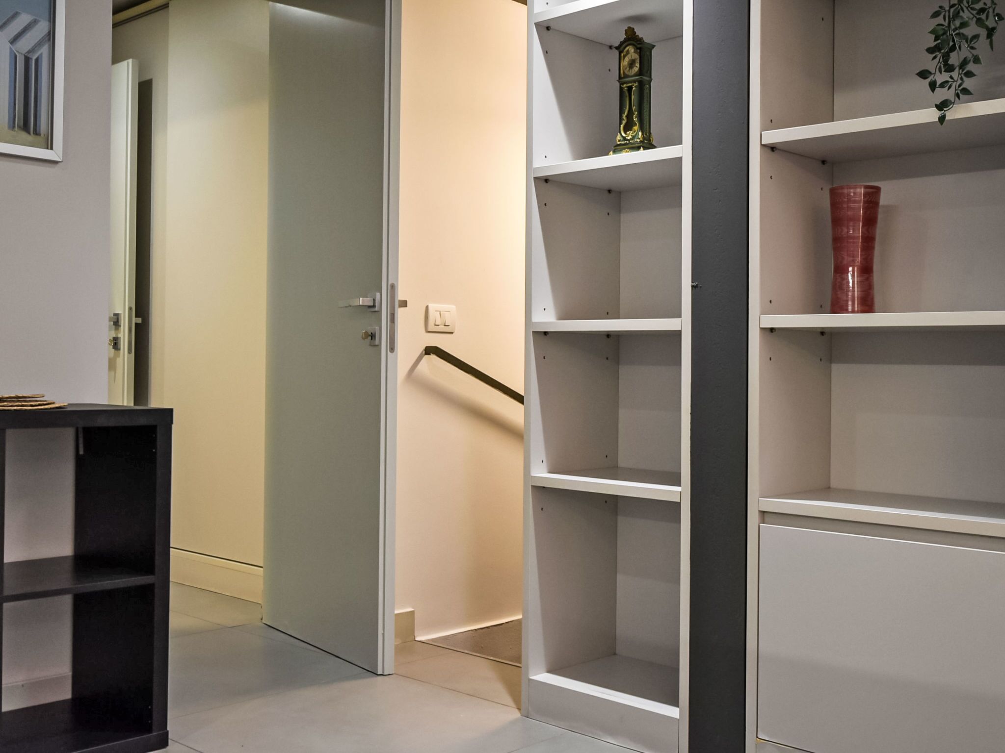 A modern interior with a closed door, a black table, and a white shelving unit with a red vase.