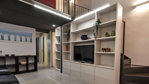 Un saló modern amb un sofà, una televisió de pantalla plana, prestatges integrats i una escala.