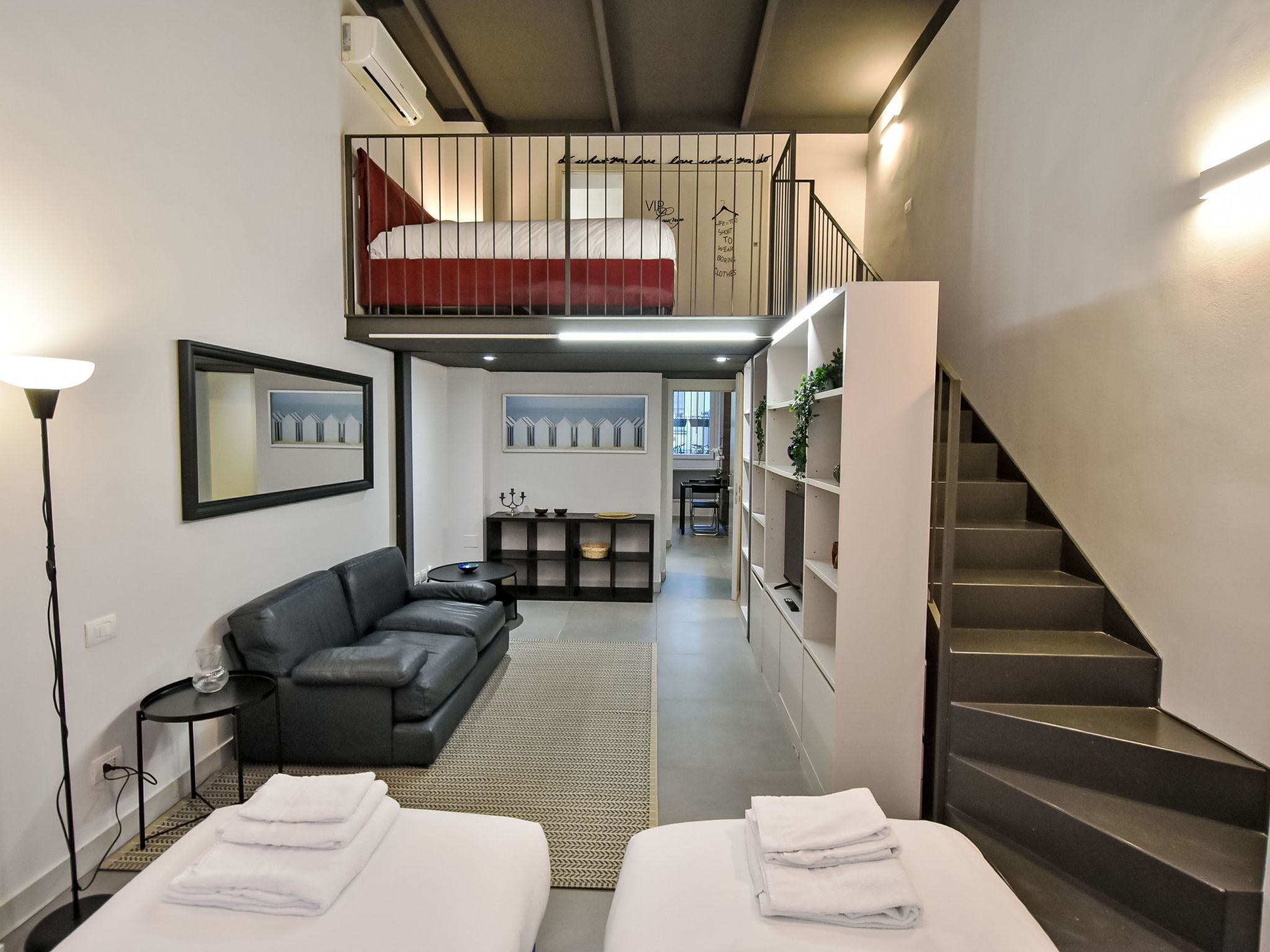 Ein modernes Hotelzimmer mit einem Hochschlafbett, einer Couch, einem Essbereich und einer Treppe.