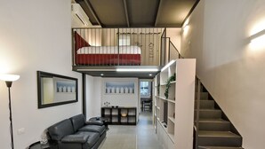 Habitació d'hotel moderna amb llit amb àtic, un sofà, zona de dinar i escala.
