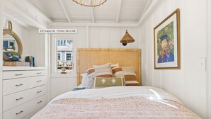 Un dormitorio con cama, cómoda, ventana y un cuadro en la pared.