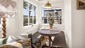Una habitación acogedora con una mesa redonda de madera, un banco y un ventanal con vistas a una casa y árboles.