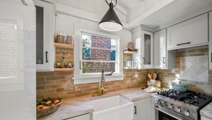 Una cocina con gabinetes blancos, una estufa a gas y una ventana que da a un muro de ladrillo.