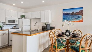 A modern kitchen with white cabinetry, a central island, and a dining area with wicker chairs.