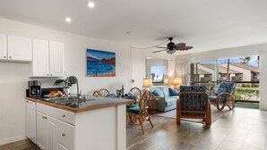 A modern kitchen with white cabinets, a dining area with wooden chairs, and a large window offering a view of a residential area.