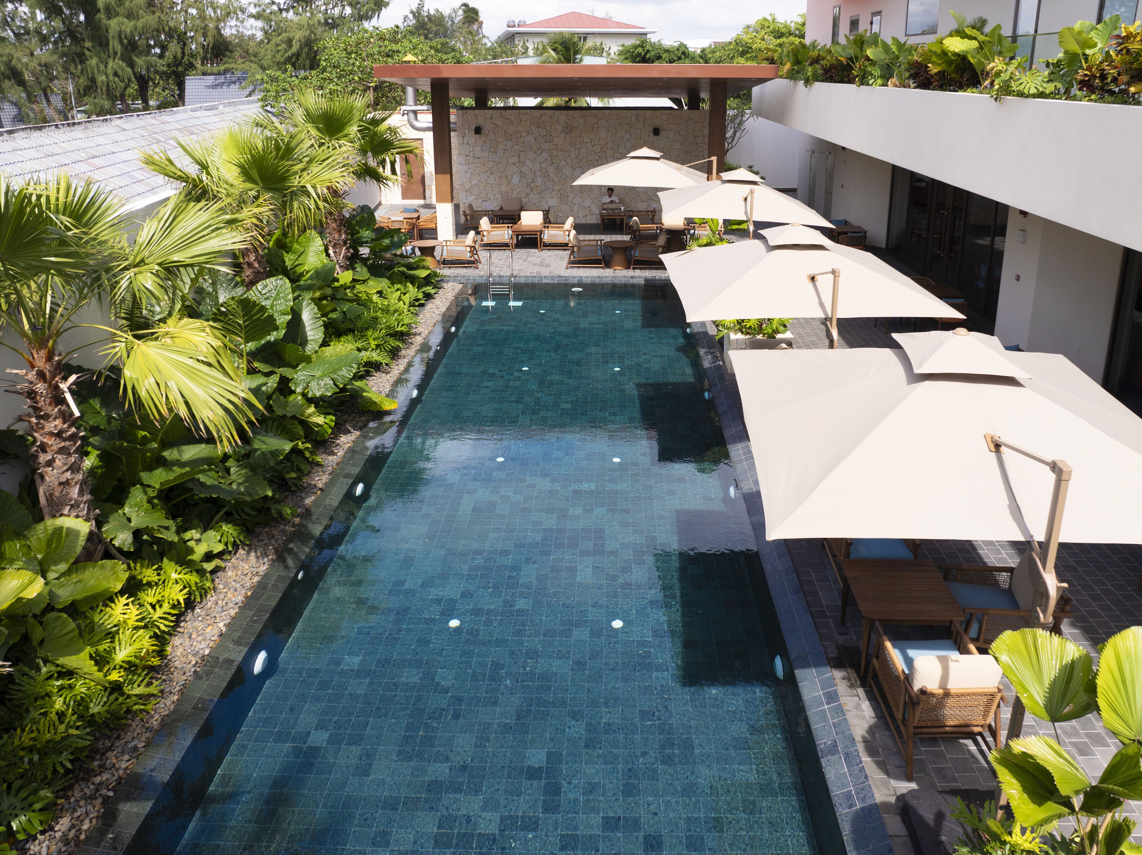 A swimming pool with lounge chairs and umbrellas, surrounded by greenery and a covered seating area.