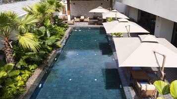 A swimming pool with lounge chairs and umbrellas, surrounded by greenery and a covered seating area.