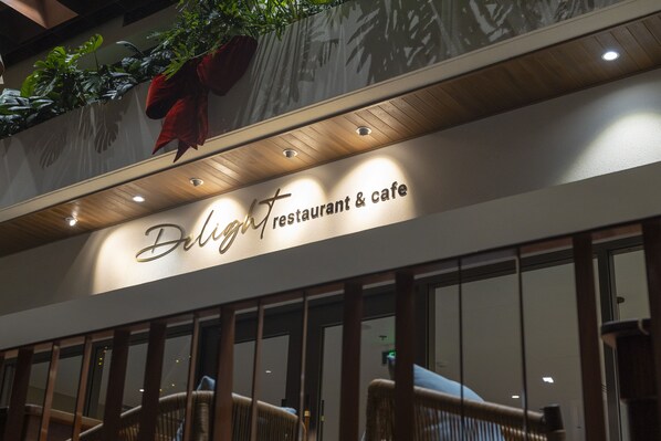 A restaurant sign with the name "Delight Restaurant & Cafe" and a decorative red bow above it.