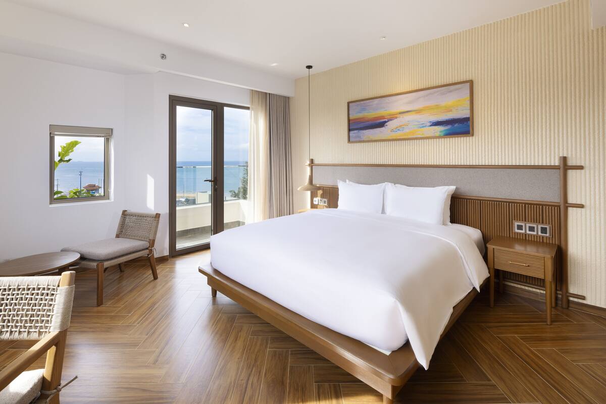 A hotel room with a large bed, a chair, a table, and a view of the ocean.