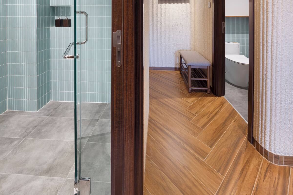 A modern bathroom with a glass shower enclosure, a wooden bench, and a large mirror.