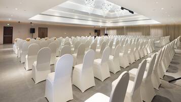 A conference room with rows of white chairs, a stage with a speaker, and a chandelier.