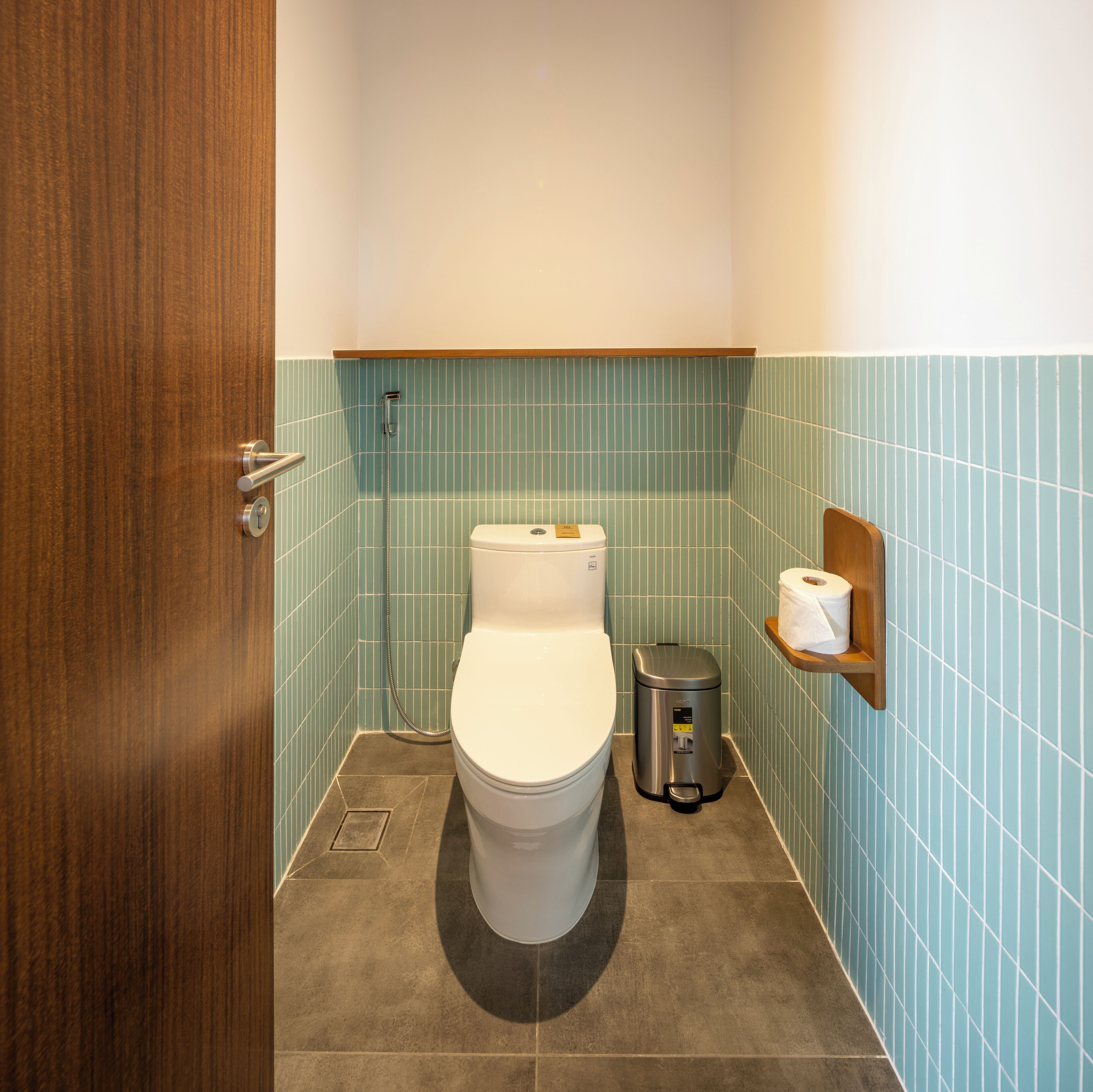 A bathroom with a toilet, a trash can, and a shelf with toilet paper.