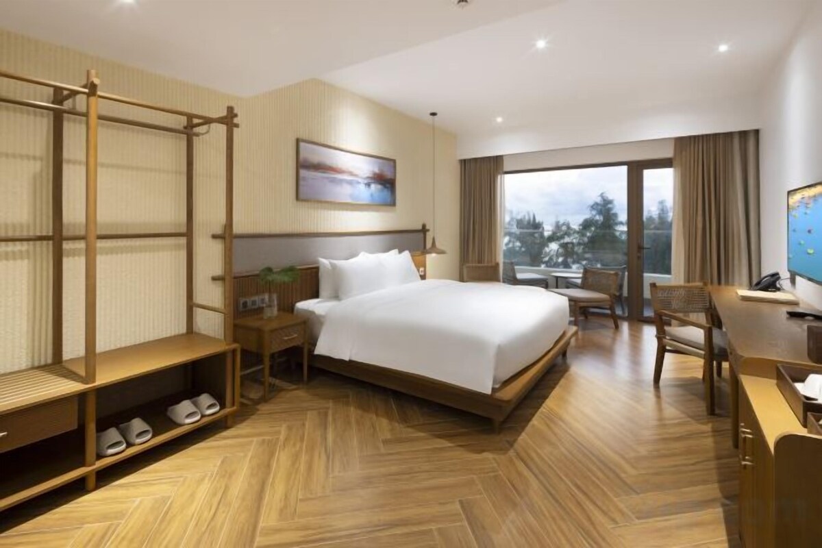 A hotel room with a large bed, a desk, a chair, a TV, and a window with a view.