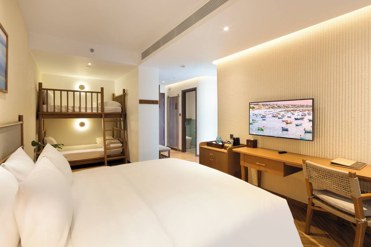 A hotel room with a large bed, a desk with a chair, a television, and a bunk bed.