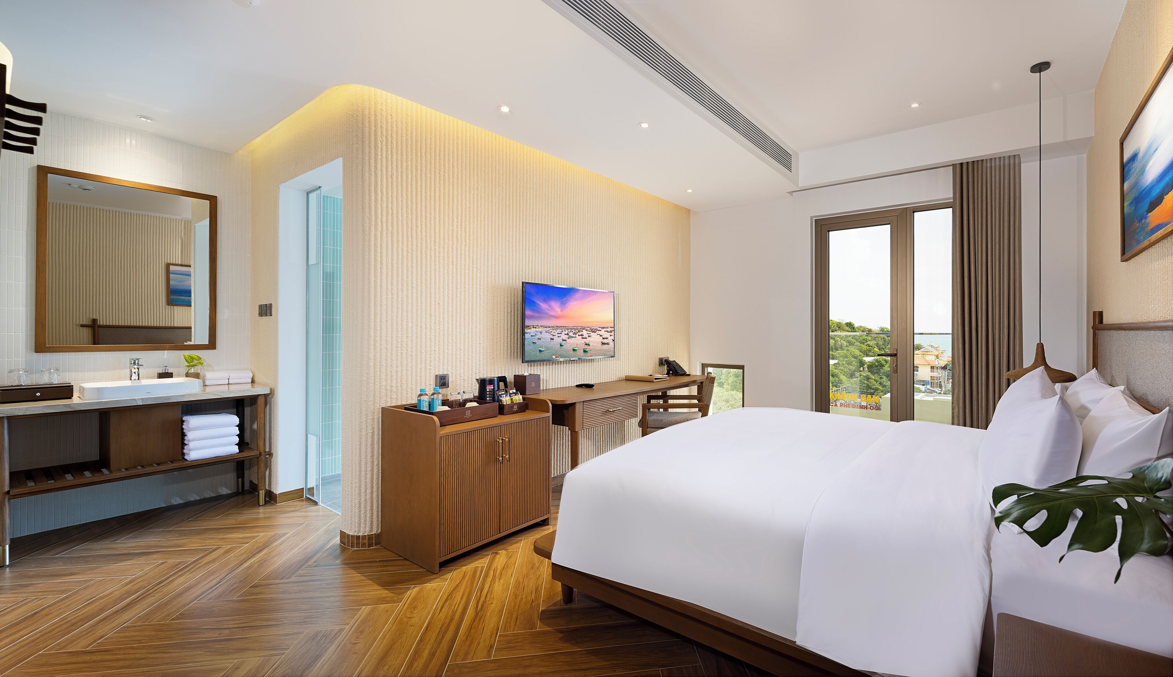 Habitación de hotel con una cama grande, un aparador de madera, un tocador con espejo, un televisor de pantalla plana y un balcón con vistas.
