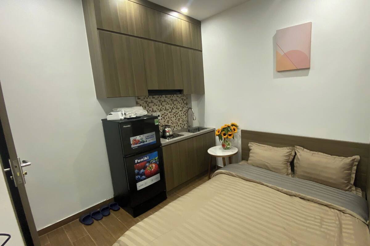 A compact bedroom with a bed, a small kitchenette, and a wall-mounted artwork.