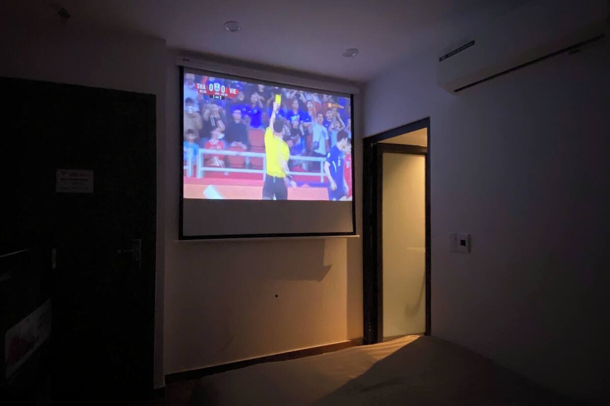 A room with a large screen displaying a sports event, a door, and a wall-mounted air conditioning unit.