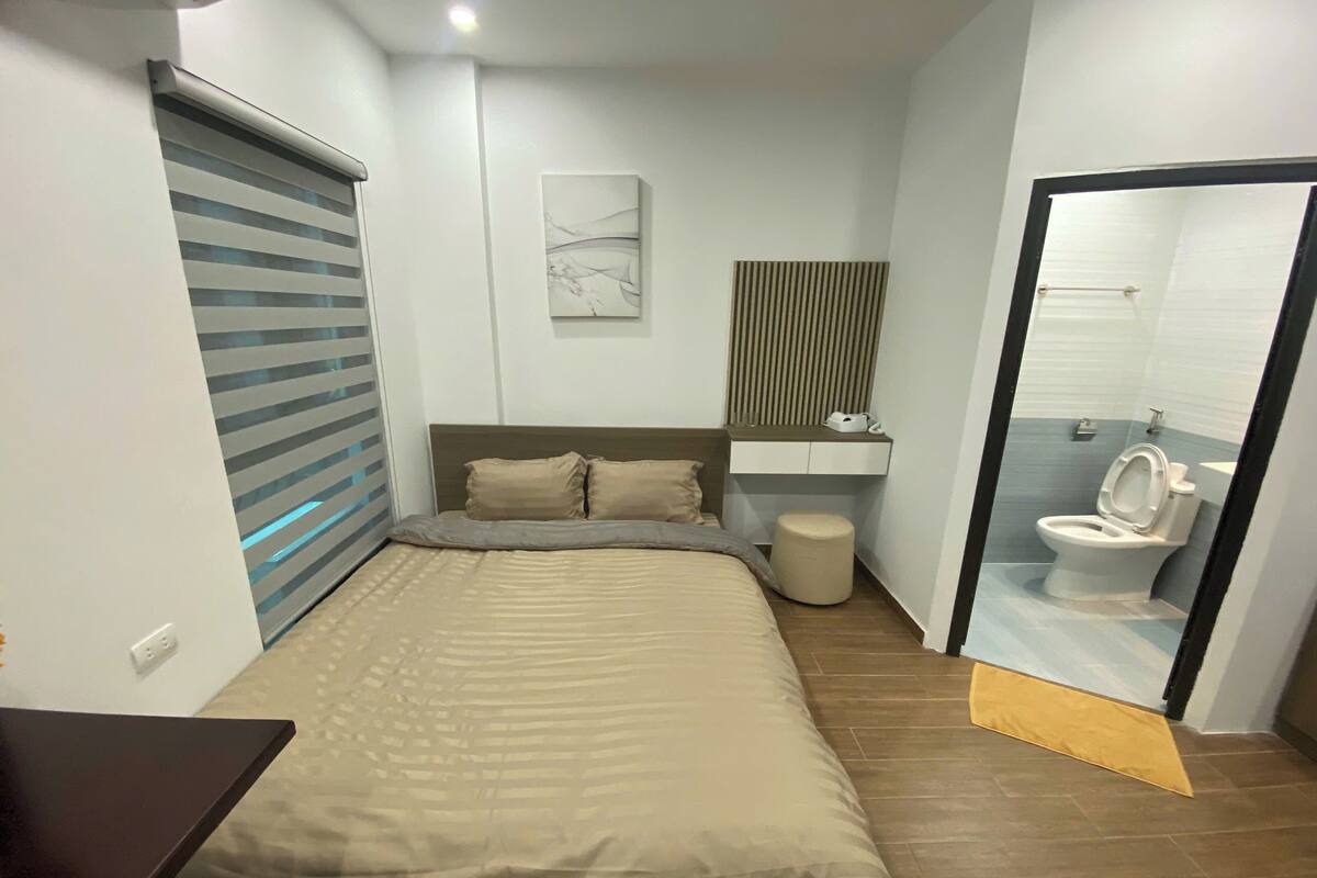 A bedroom with a bed, bedside table, and a bathroom with a toilet and sink.