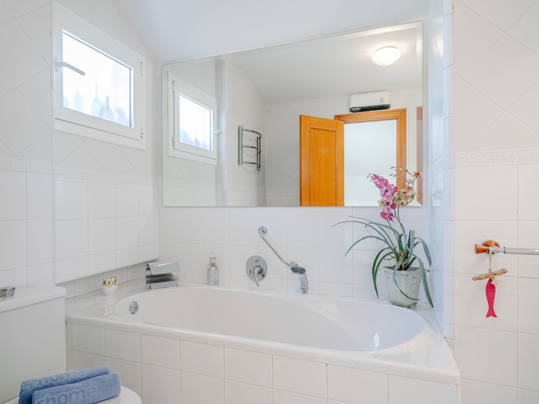 A modern bathroom with a large bathtub, a sink, and a mirror. There is a window above the sink and a potted plant on the right side.