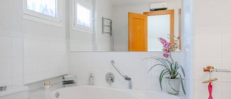 A modern bathroom with a large bathtub, a sink, and a mirror. There is a window above the sink and a potted plant on the right side.